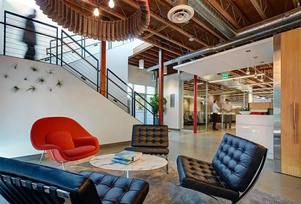 Double-height office lobby with lounge chairs beneath an open staircase